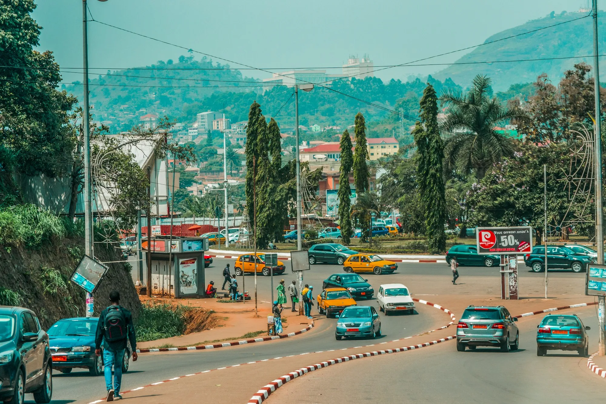 Traffic, taxis and pedestrians at the Nlongkak roundabout in Yaoundé with green hills behind