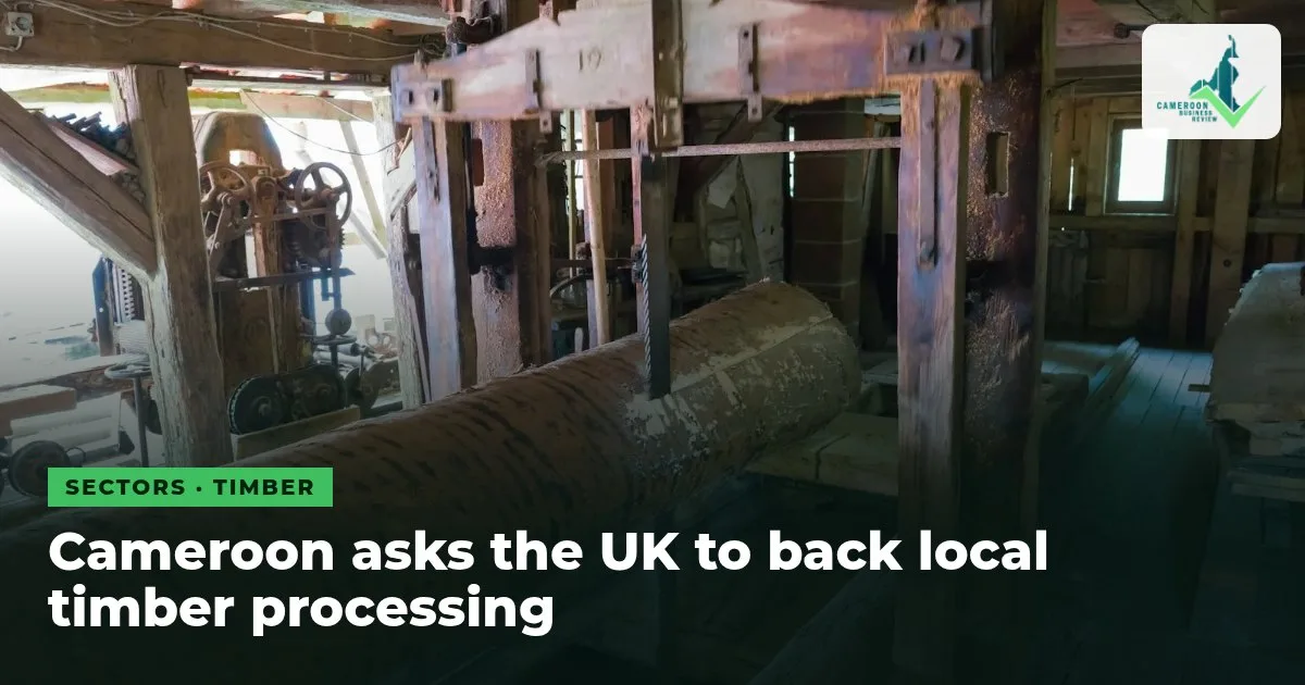 A log on the carriage of an old sawmill, with wooden beams and machinery around it, under the headline Cameroon asks the UK to back local timber processing